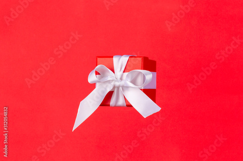 Red gift box with white satin ribbon bow flying on red background. Minimal concept for christmas holidays, birthday, valentine, shopping and sales.