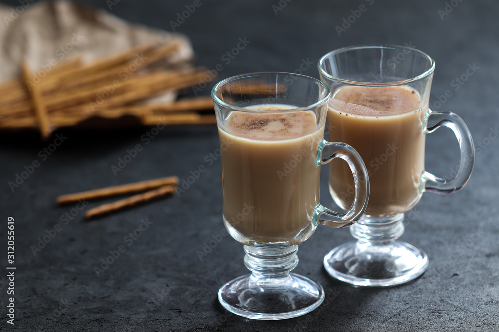 Indian masala tea with milk, spices and cinnamon and biscuits straws on a dark gray background Indian masala tea with milk, spices and cinnamon and biscuits straws on a dark gray background
