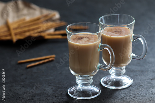 Indian masala tea with milk, spices and cinnamon and biscuits straws on a dark gray background