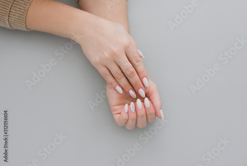 Beautiful stylish female manicure on a gray background with gift in hand.