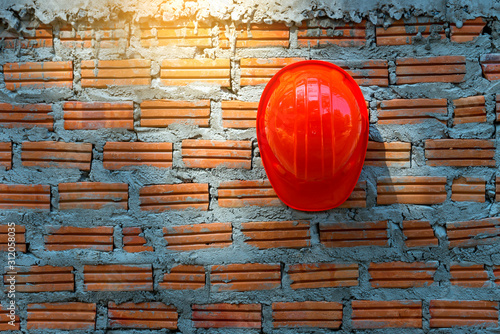 Orange Engineer hat hanging on a brick wall construction.