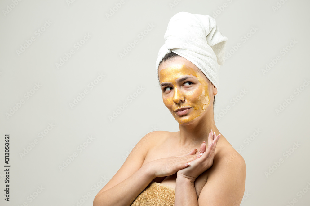 Beauty portrait of woman in white towel on head with gold nourishing mask on face. Skincare cleansing eco organic cosmetic spa relax concept. Beauty portrait of woman in white towel on head with gold nourishing mask on face. Skincare cleansing eco organic cosmetic spa relax concept.