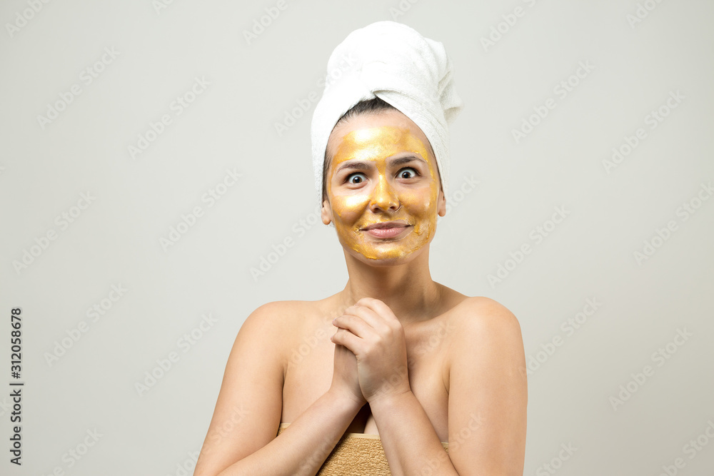Beauty portrait of woman in white towel on head with gold nourishing mask on face. Skincare cleansing eco organic cosmetic spa relax concept. Beauty portrait of woman in white towel on head with gold nourishing mask on face. Skincare cleansing eco organic cosmetic spa relax concept.