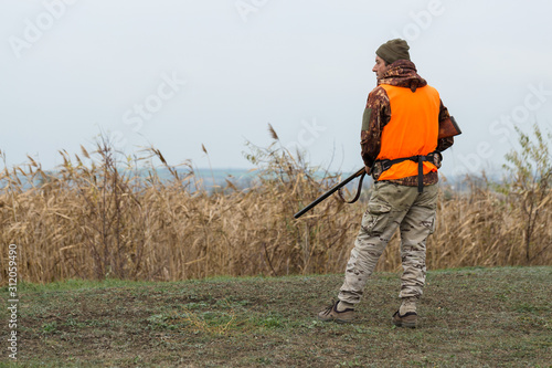 Hunting period, autumn season open. A hunter with a gun in his hands in hunting clothes in the autumn forest in search of a trophy. © Mountains Hunter