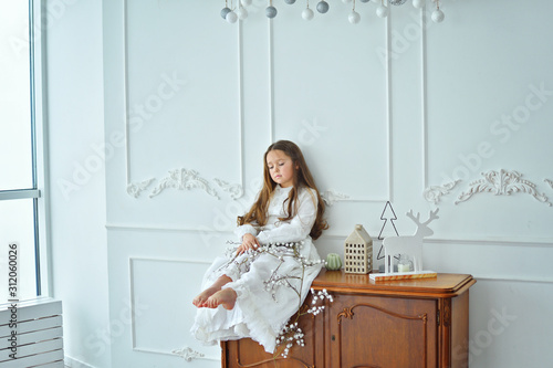 Cute long-haired girl in a white retro dress and with Christmas decor. Happy New Year