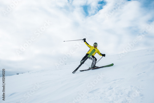 excited sportsman holding ski sticks and skiing on white slope
