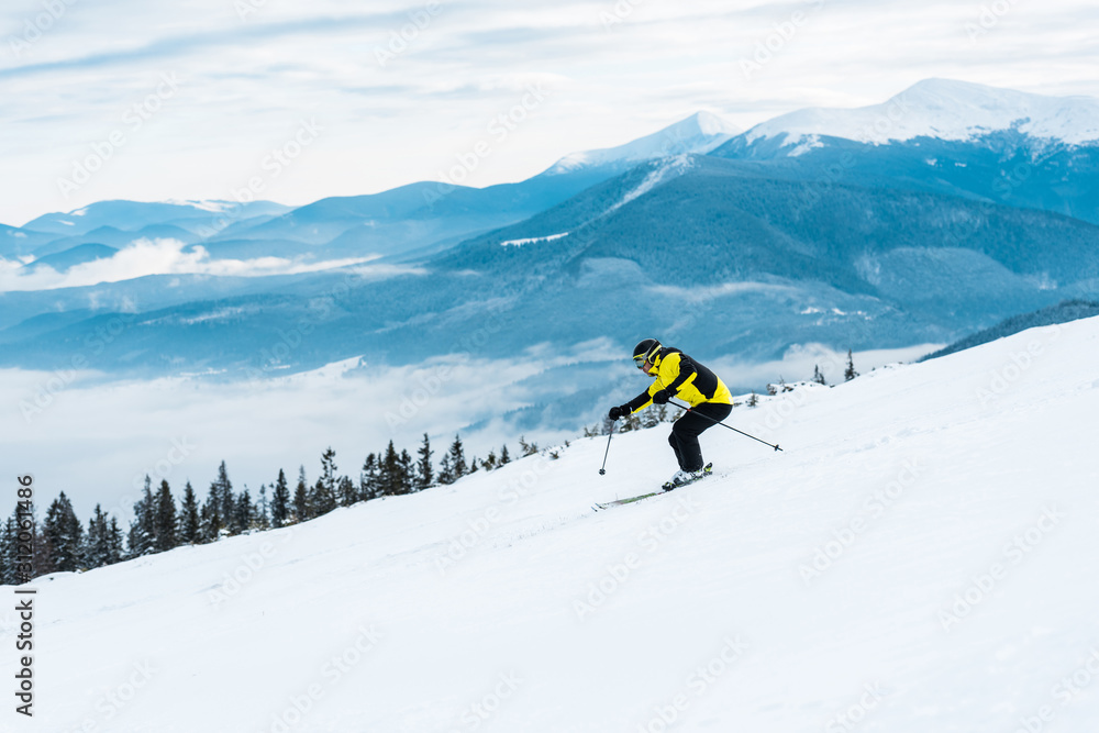 sportsman holding sticks and skiing on slope with snow in mountains
