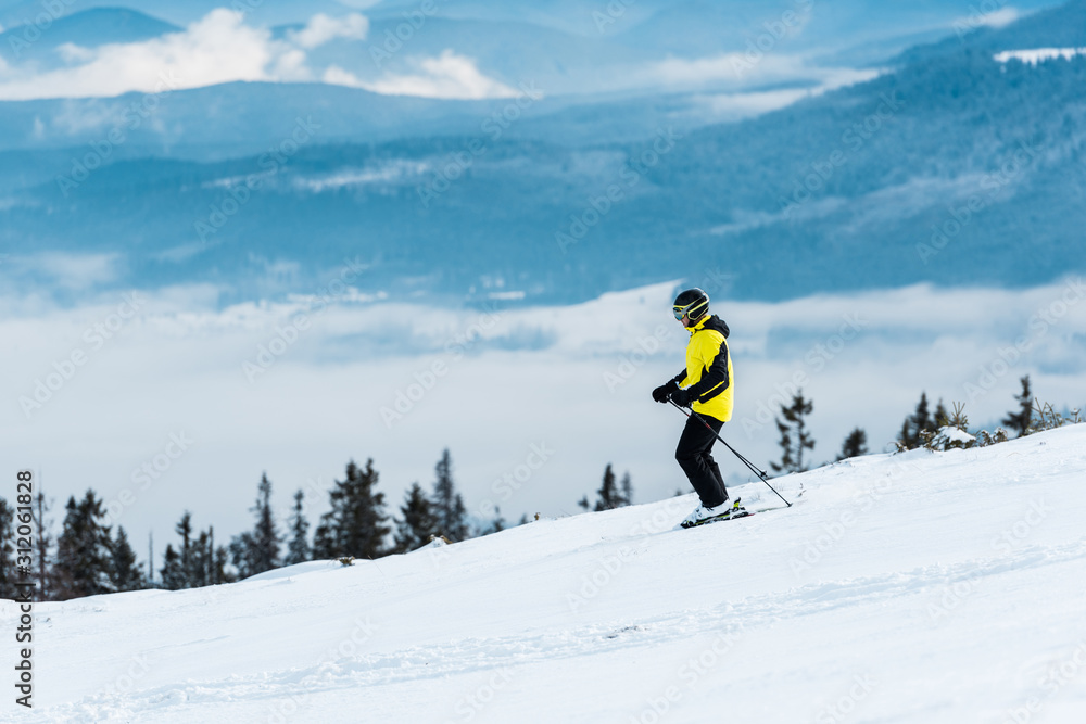 skier in helmet holding sticks and skiing on slope in wintertime