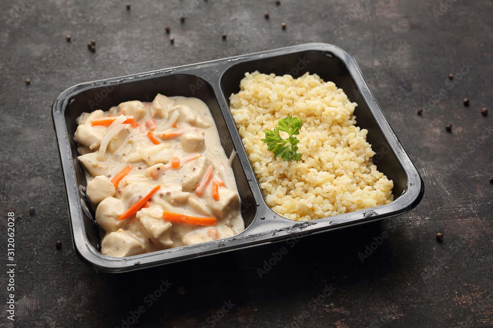Box diet. Chicken in mustard cream sauce with bulgur groats. Ready dish in a black container. Composed take-out meal, diet catering. The container on a dark background. Box diet. Chicken in mustard cream sauce with bulgur groats. Ready dish in a black container. Composed take-out meal, diet catering. The container on a dark background.