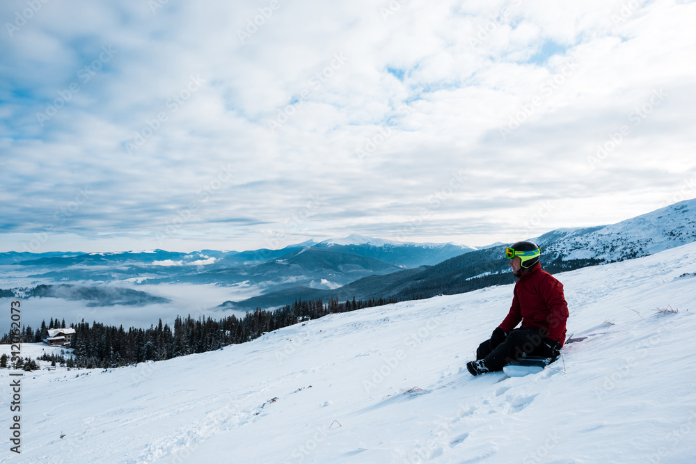 snowboarder in helmet sitting on slope against blue sky