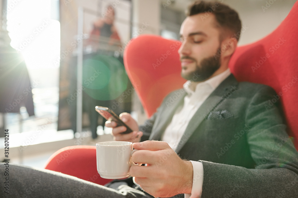 Hand of young well-dressed businessman with cup of tea relaxing in red armchair Hand of young well-dressed businessman with cup of tea relaxing in red armchair