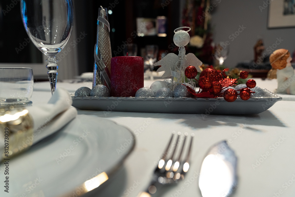 Christmas table with a white tablecloth, crystal glasses, pieces of cutlery, red candles and christmas decoration.