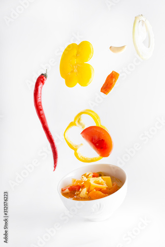 vegetable Lecho of tomatoes, sweet peppers, carrots, onions, garlic, on a white background, flying pieces of vegetables,