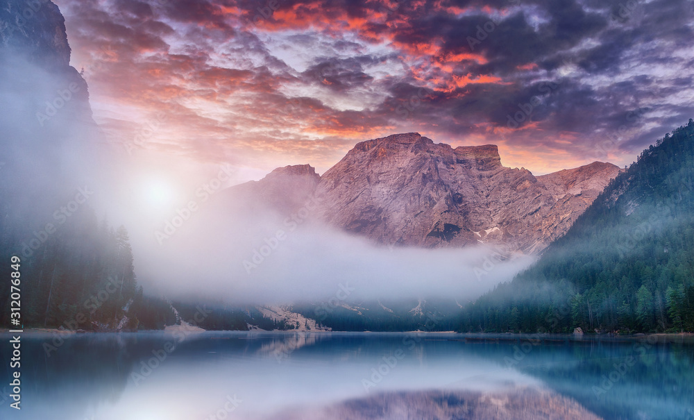 Naklejka premium Beautiful natural landscape. Fairy-tale Foggy Morning in mountain valley. Fantastic Colorful sky over the Braies Lake at Dolomites Alps during sunset. Beautiful locations of the World. postcard.