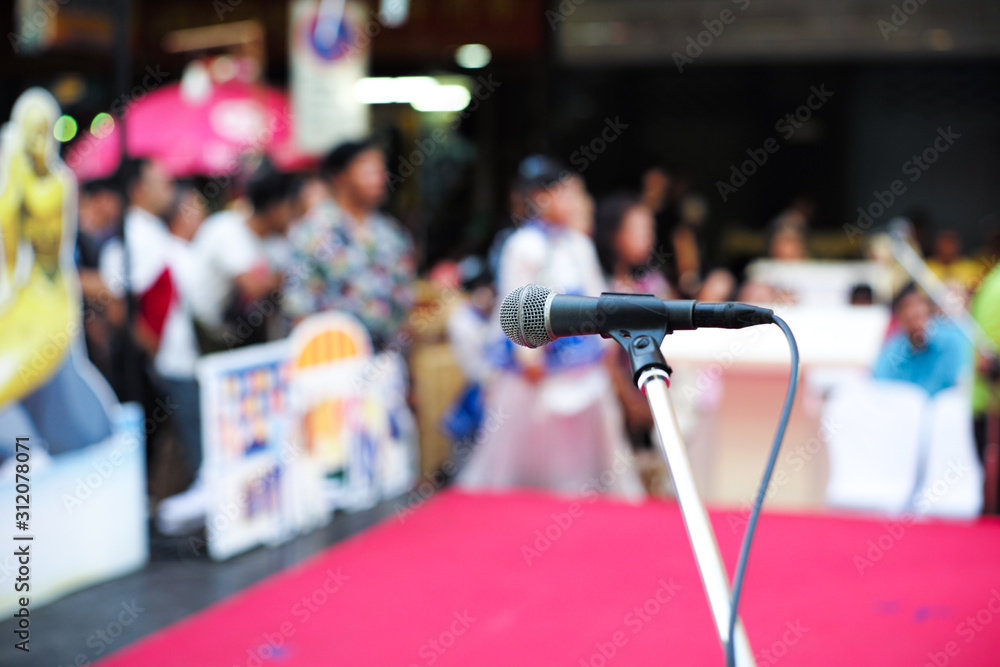 Selective focus on microphone on stage with blurred crowd of people in background