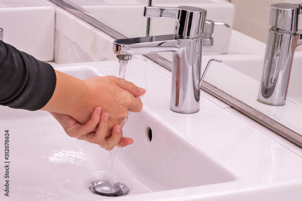 Young girl is washing her hands under pouring water from tap in water closet room with mirror. Concept of self hygiene and cleanliness Young girl is washing her hands under pouring water from tap in water closet room with mirror. Concept of self hygiene and cleanliness