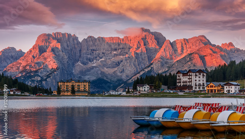 Misurina Lake with colorful sky during sunrise. Wonderful Nature landscape. View on lake with boats and Majestic mountains peak in clouds, on background. Famous World place. Creative image