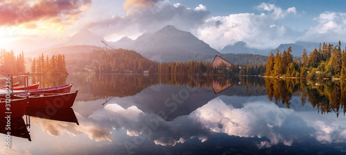 Fototapeta Naklejka Na Ścianę i Meble -  Incredible Nature Landscape. Beautiful view of traditional wooden boats on  Strbske Pleso Lake during sunset. Awesome Sunny natural scene. Popular travel and hiking destination. Beautiful on the World