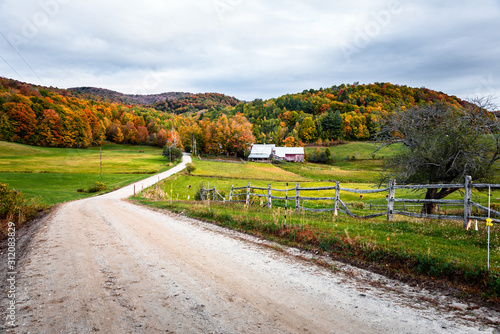 Unpaved road to a farm in a rolling rural landscape on a cloudy autumn morning. Beautiful autumn colours.