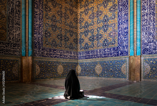 Unidentified Iranian woman wearing chador praying inside Sheikh Lotfollah Mosque with tiles on walls, Isfahan, Iran photo