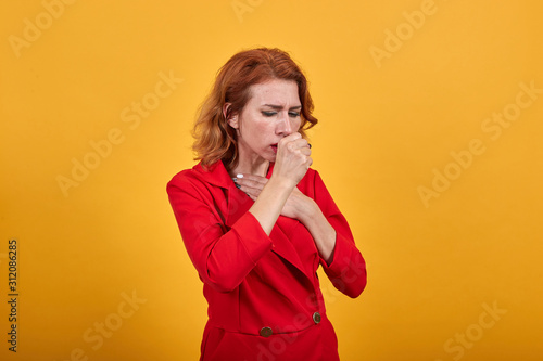 Sickness caucasian young woman cough, keeping fist on mouth, wearing fashion red jacket over isolated orange background. People lifestyle concept.