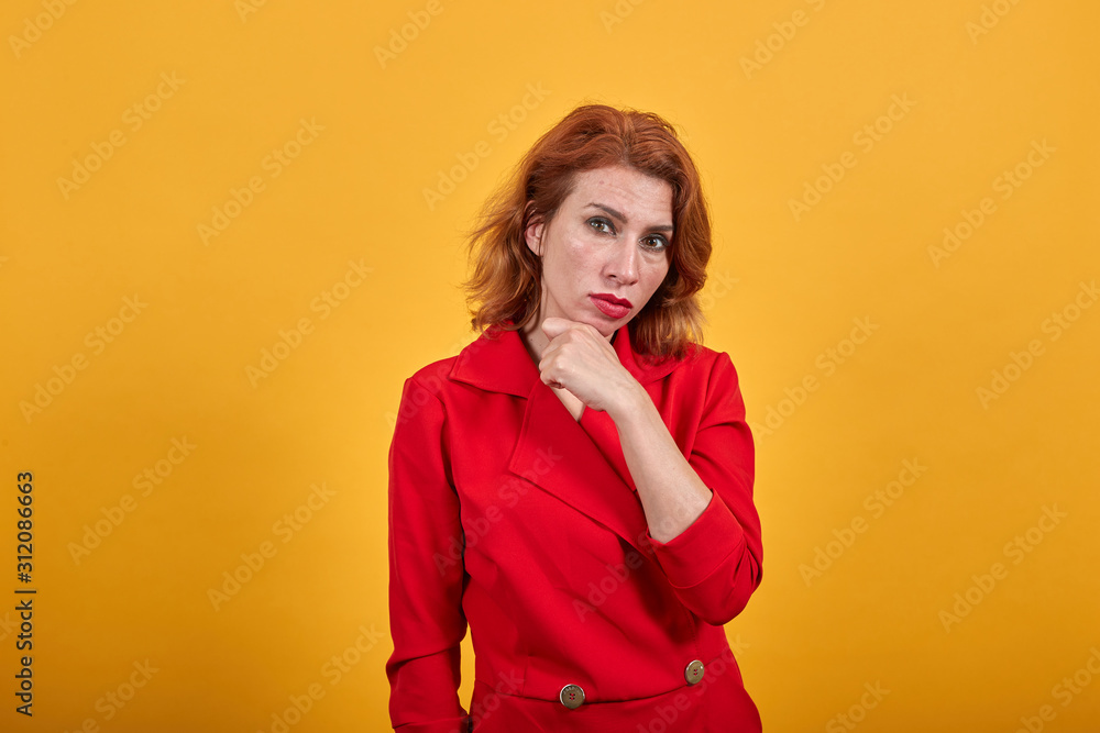Serious caucasian young woman keeping hand on chin, looking up, thinking about issue wearing fashion red jacket over isolated orange background. People lifestyle concept. Serious caucasian young woman keeping hand on chin, looking up, thinking about issue wearing fashion red jacket over isolated orange background. People lifestyle concept.