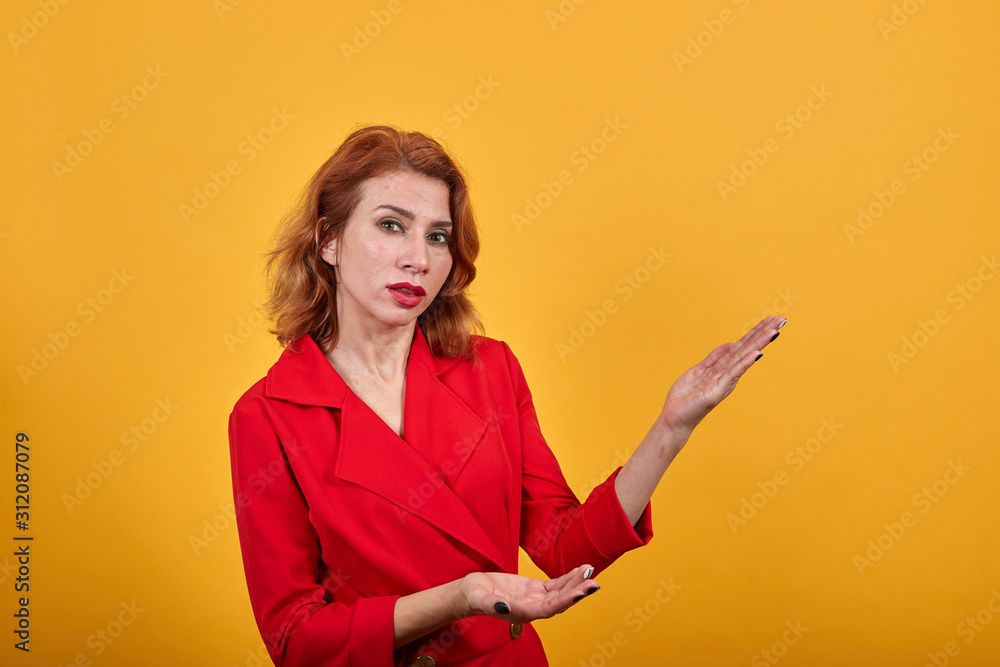 Serious charming caucasian young woman pointing hands aside, looking directly wearing fashion red jacket over isolated orange background. People lifestyle concept. Serious charming caucasian young woman pointing hands aside, looking directly wearing fashion red jacket over isolated orange background. People lifestyle concept.