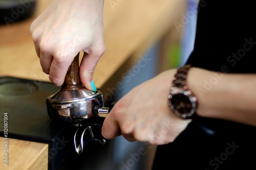 Woman hand holding a portafilter with morning coffee. Waiter making latte. Preparation cappuccino.Service. Cafe. Barista hands holding portafilter and coffee tamper making an espresso coffee.