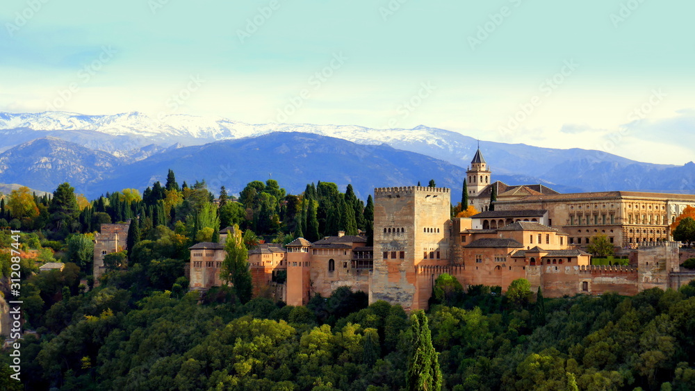 im Abendlicht erleuchtete Burg Alhambra mit schneebedeckter Sierra Nevada im Hintergrund