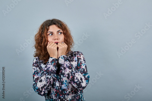 Scared charming young lady bitting nails, having nice ring over isolated gray background in fashion shirt. People emotions. Lifestyle concept