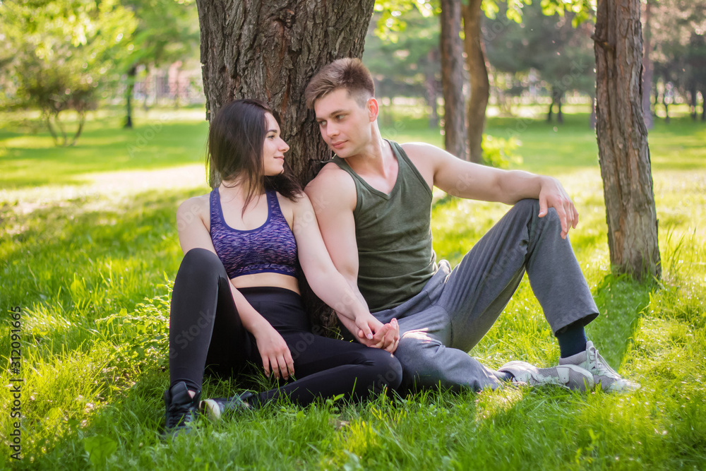 Athletic guy and girl sitting on the lawn leaning against a tree. Athletic guy and girl sitting on the lawn leaning against a tree.