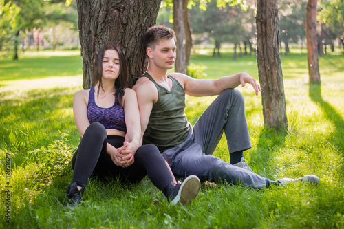 Athletic guy and girl sitting on the lawn leaning against a tree.