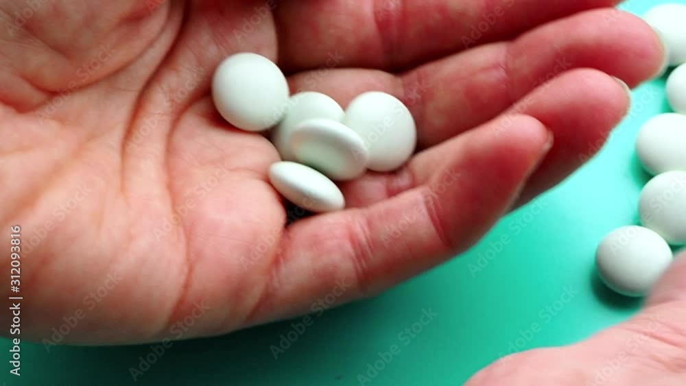 The woman puts a lot of pills in the palm of her hand. The concept of overdose, medicine and health care. A dose for death. Excess of drugs in modern treatment. Capsules on a blue background The woman puts a lot of pills in the palm of her hand. The concept of overdose, medicine and health care. A dose for death. Excess of drugs in modern treatment. Capsules on a blue background