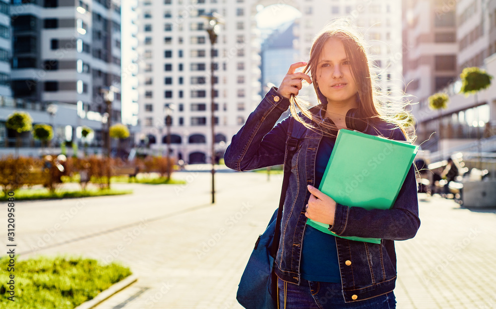 Fototapeta premium Back to school student teenager girl holding books and note books wearing backpack. Outdoor portrait of young teenager brunette girl with long hair. girl on city