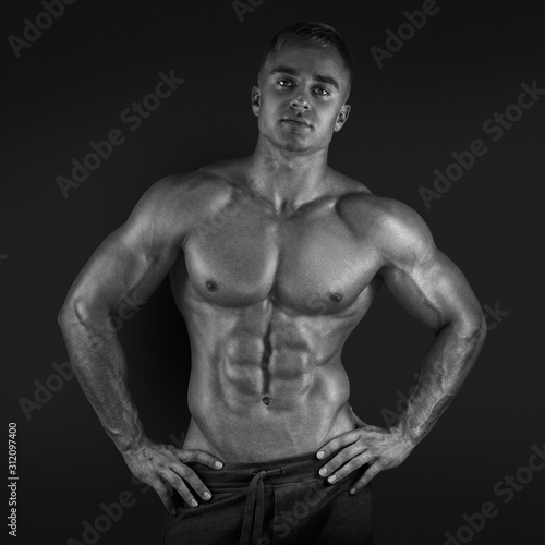 Sexy shirtless male model posing Muscular and fit bodybuilder fitness male model posing over black background. Strong and handsome young man demonstrate his muscular torso. Black and white photo.