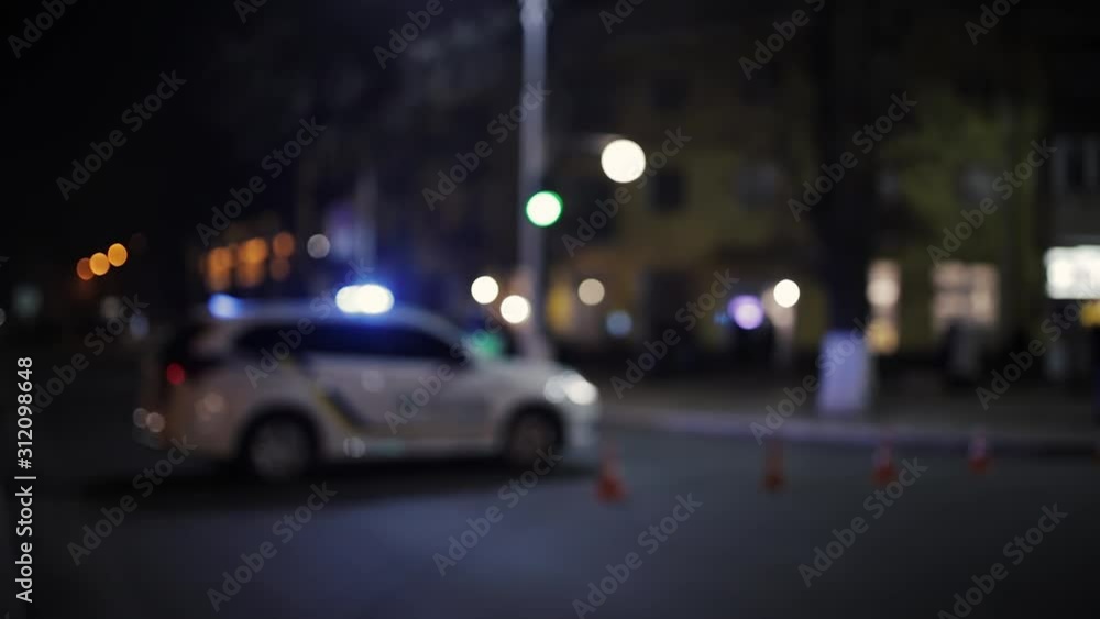 Unfocused shot of police car with sirens and traffic cones on city road. Emergency or crime scene. Night lights bokeh. Unfocused shot of police car with sirens and traffic cones on city road. Emergency or crime scene. Night lights bokeh.