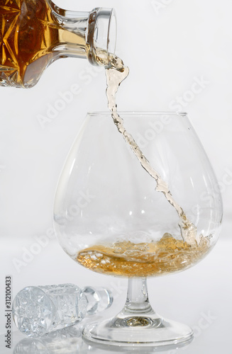 Decanting cognac into a brandy snifter on white background