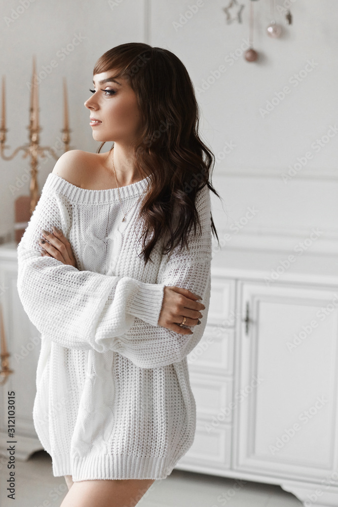Happy young brunette woman with perfect slim body in warm cozy sweater dreaming, looking down. Cozy winter portrait of fashionable model girl with tender makeup posing in interior. Beauty and fashion Happy young brunette woman with perfect slim body in warm cozy sweater dreaming, looking down. Cozy winter portrait of fashionable model girl with tender makeup posing in interior. Beauty and fashion