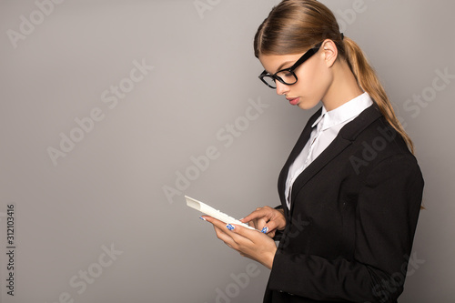 businesswoman in glasses using calculator isolated on grey