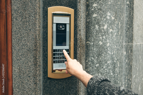 A female hand presses the buttons on the intercom for access inside photo