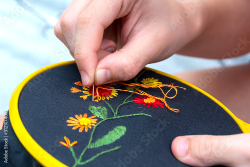 Women's hand embroidery in a hoop, a woman embroider a pattern on dark material. Close-up. The concept of needlework, hobby, leisure. photo