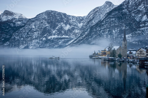 a ferry on the lake passing by the foggy mountains with snow on the trees in winter
