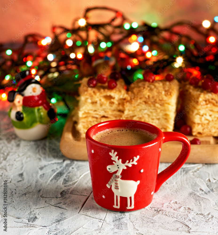 red ceramic cup with black coffee. near green branches of spruce and christmas toys