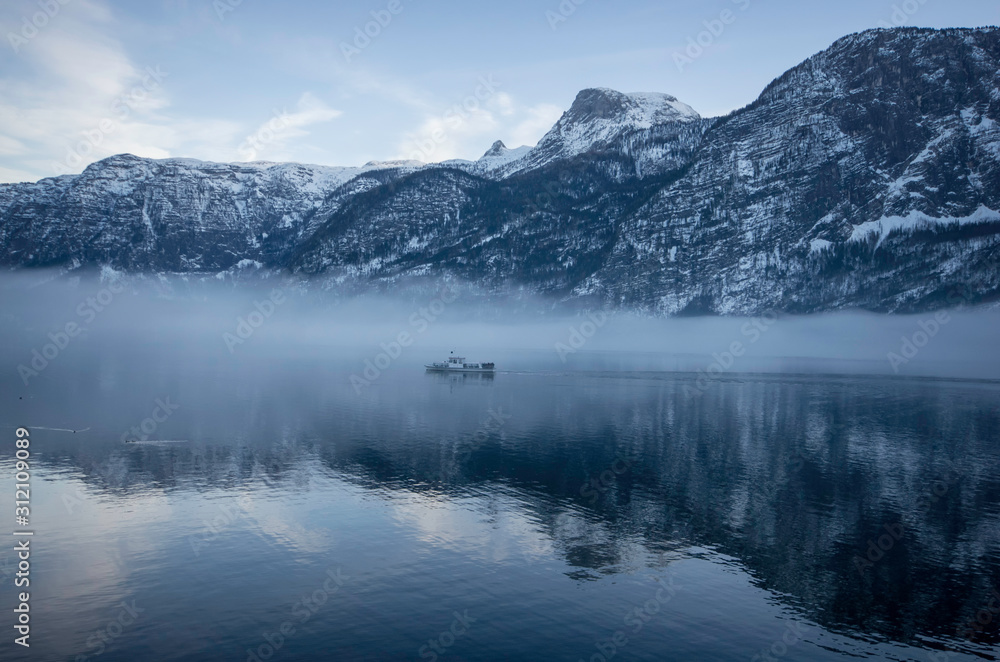 a ferry on the lake  passing by the foggy mountains with snow on the trees in winter
