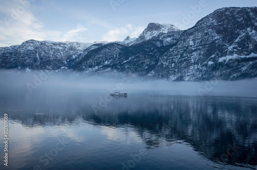 a ferry on the lake passing by the foggy mountains with snow on the trees in winter