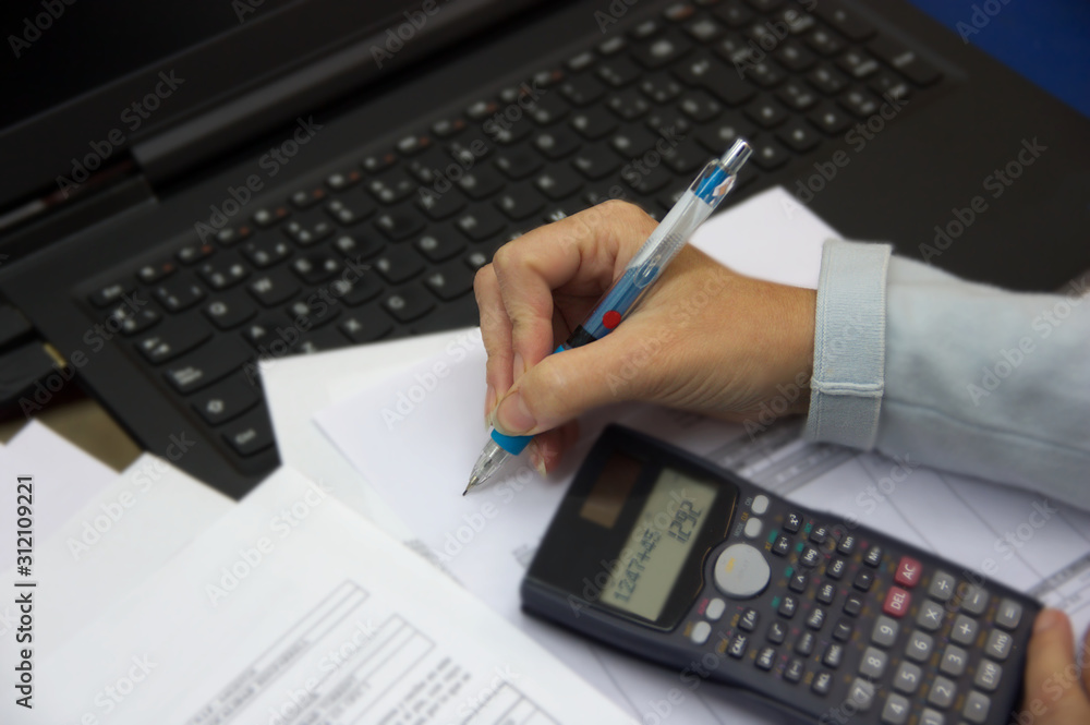 Someone writes on a paper next to a laptop and a calculator Someone writes on a paper next to a laptop and a calculator