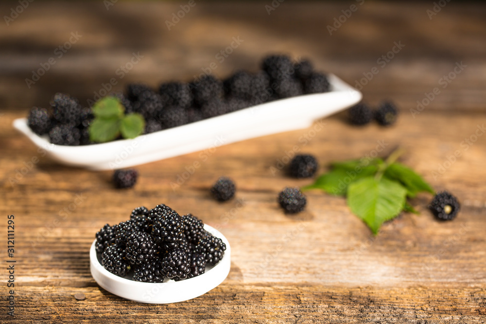 Ripe blackberries with leaves in a bowl on a woodenk background Ripe blackberries with leaves in a bowl on a woodenk background