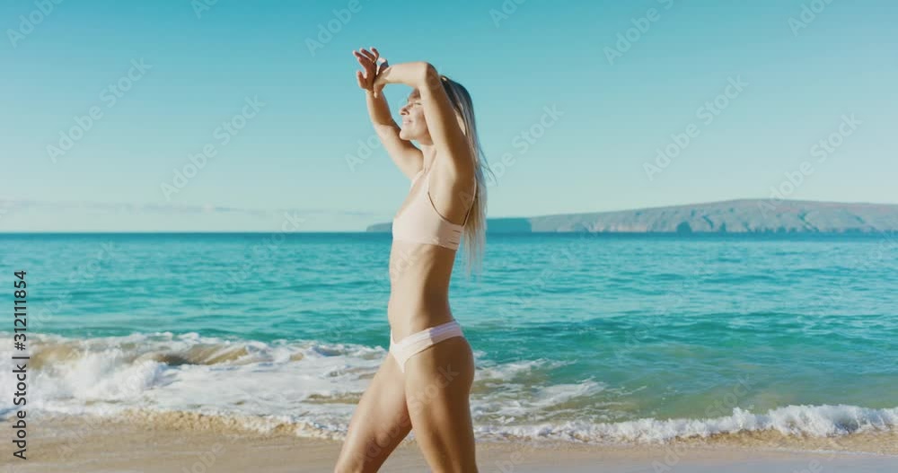 Happy attractive woman walking on the beach smiling and looking back, young active woman in a bikini enjoying a walk on the beach on a sunny day Happy attractive woman walking on the beach smiling and looking back, young active woman in a bikini enjoying a walk on the beach on a sunny day