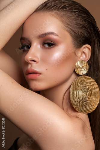 A photo of the young girl with professional make-up, perfect skin, round gold earrings in fashion pose.