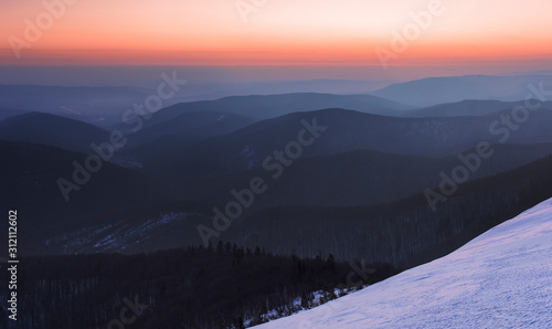 Fototapeta Naklejka Na Ścianę i Meble -  Winter Carpathians. Morning twilight on mountain ridges covered with deciduous forest with orange sky on the horizon. Morning twilight in the winter Carpathians. Beskidy area.